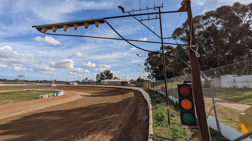 Old rusted light poles and a traffic light around a dirt speedway.