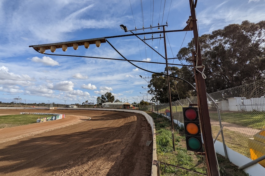 Old rusted light poles and a traffic light around a dirt speedway.