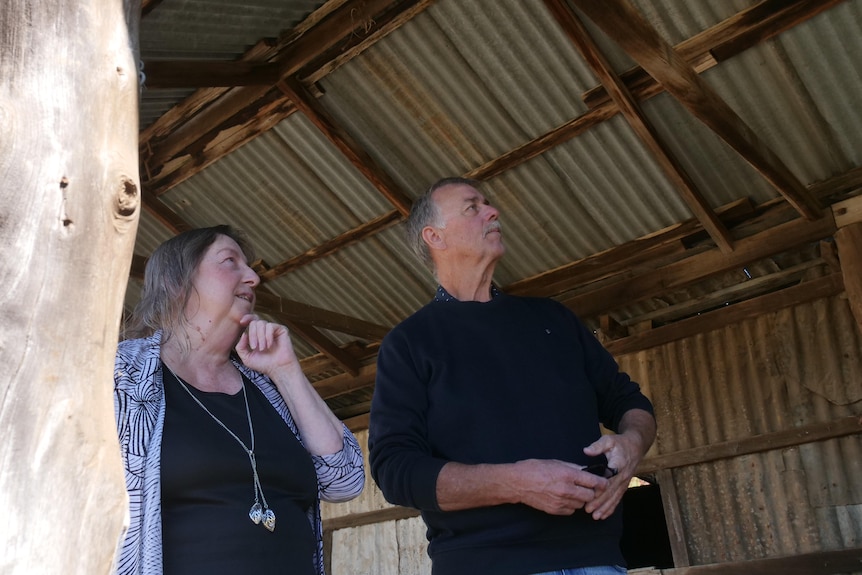 A man and woman look at an old stable building featuring old timber. 