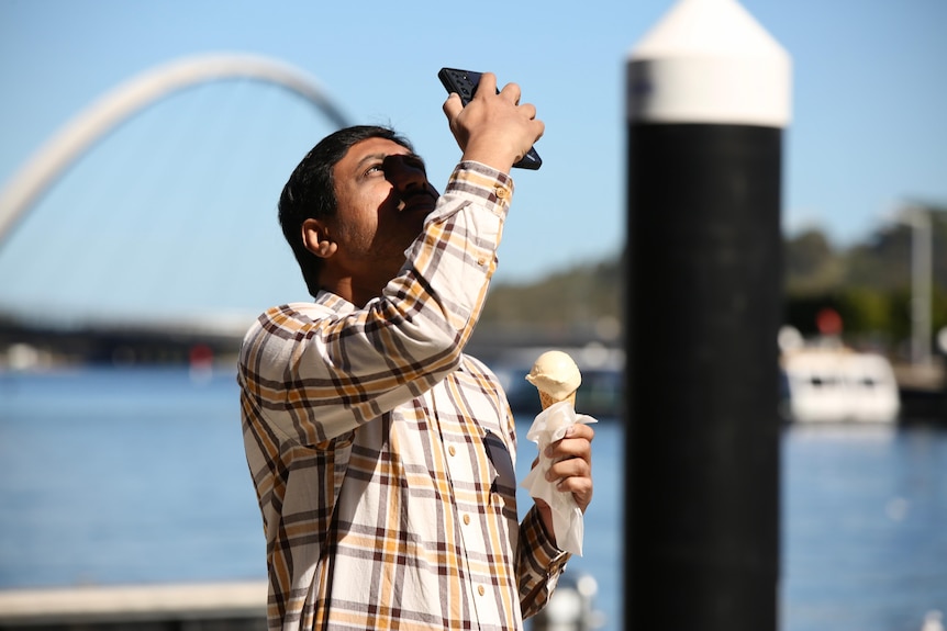 A man holds an ice cream while looking up at the sky.