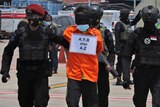 Armed police escort a suspected militant wearing an orange jumpsuit and blindfolded.