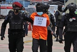 Armed police escort a suspected militant wearing an orange jumpsuit and blindfolded.