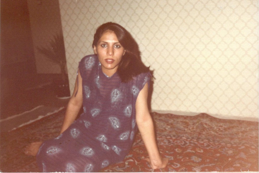 Medium archive shot of a woman sitting on carpet facing the camera.
