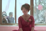 Colour still of Gai Qi seated and wearing a red wedding dress in a bedroom with people looking in through the window.