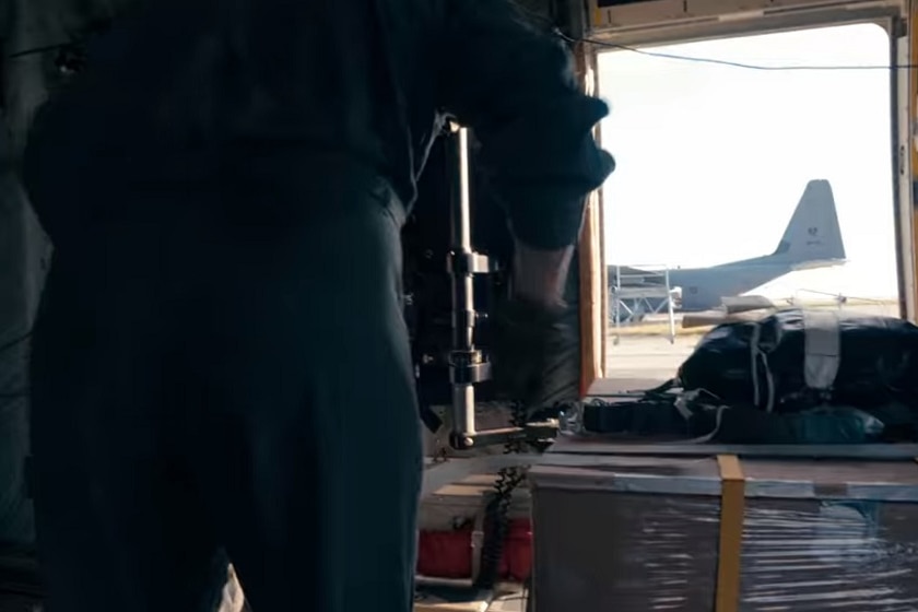 A uniformed person pushes a large crate through the interior of a Defence plane