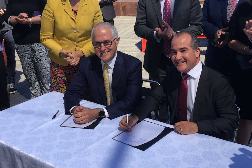 Malcolm Turnbull and James Merlino sign documents together at a media conference.