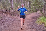 A woman gives the peace sign while running on a bush track.