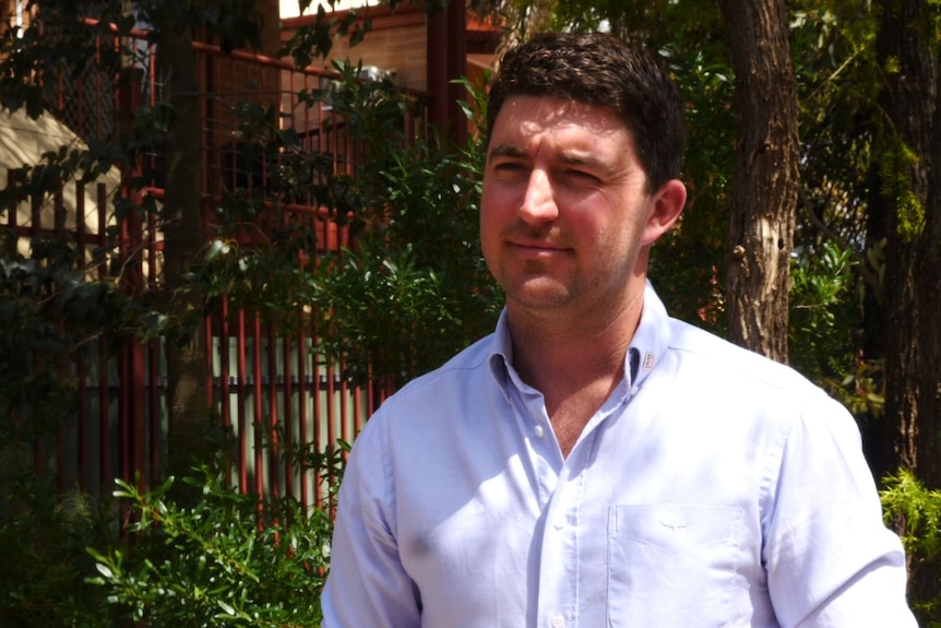 mid shot of man in business shirt standing in front of bushes