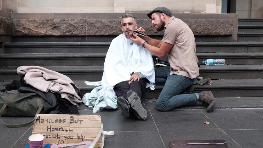 Joshua Coombes shaving a man's face and cutting his hair on the street in Melbourne.