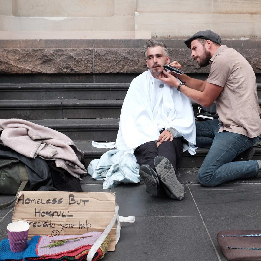 Joshua Coombes shaving a man's face and cutting his hair on the street in Melbourne.