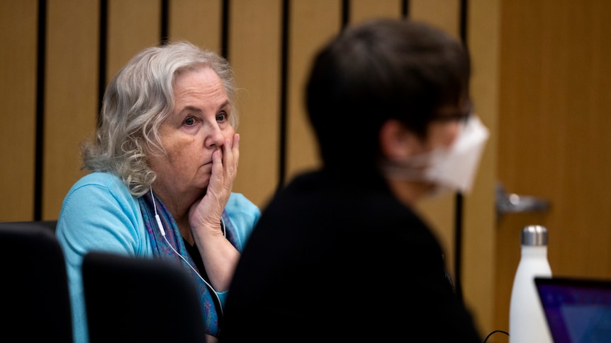 A woman sits in a court room with her head leaning on her palm