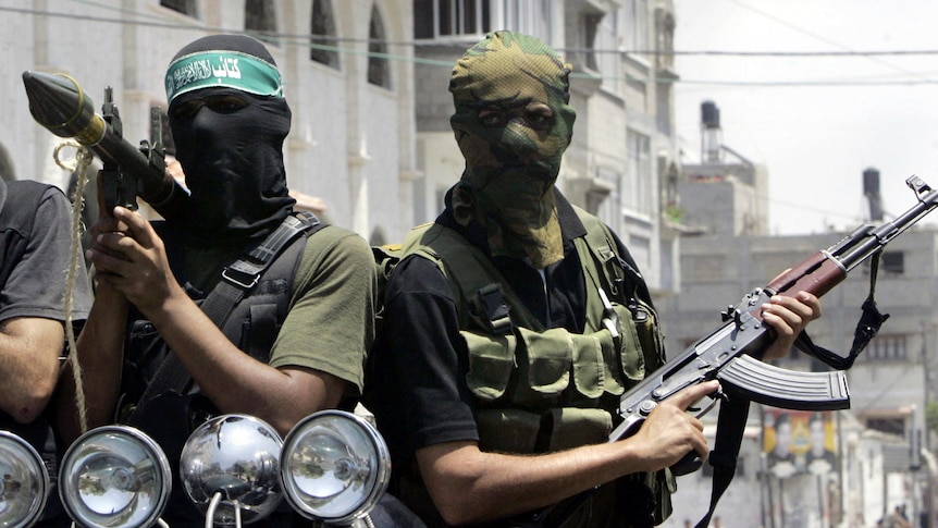Hamas militants with their faces covered with masks on the back of a truck holding weapons. 