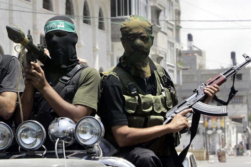 Hamas militants with their faces covered with masks on the back of a truck holding weapons. 