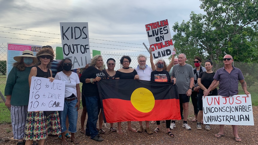 a group of protesters holding signs and an Aboriginal flag