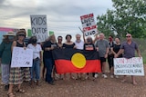 a group of protesters holding signs and an Aboriginal flag
