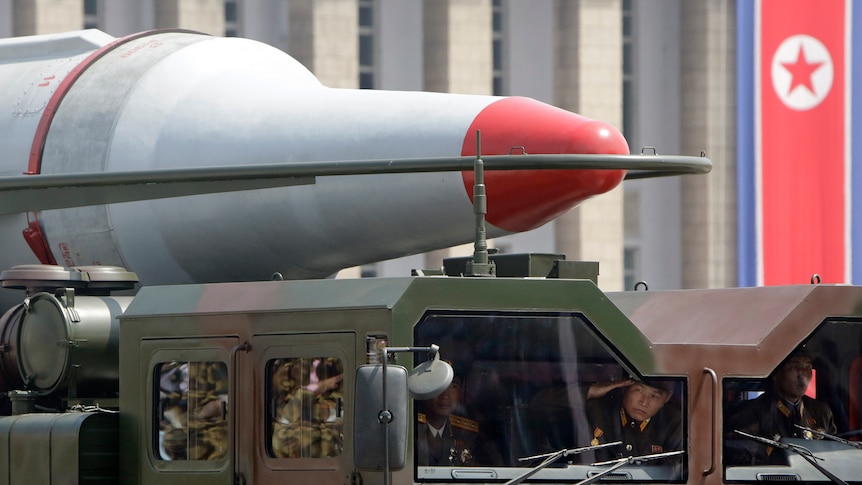 North Korean soldiers salute in a military vehicle carrying a missile during a parade.