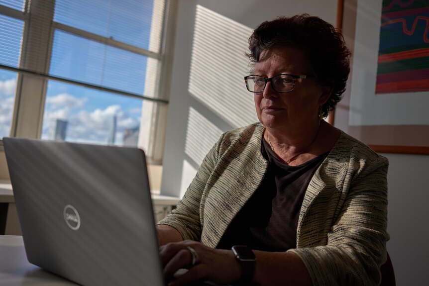 A woman with glasses sitting down at a laptop