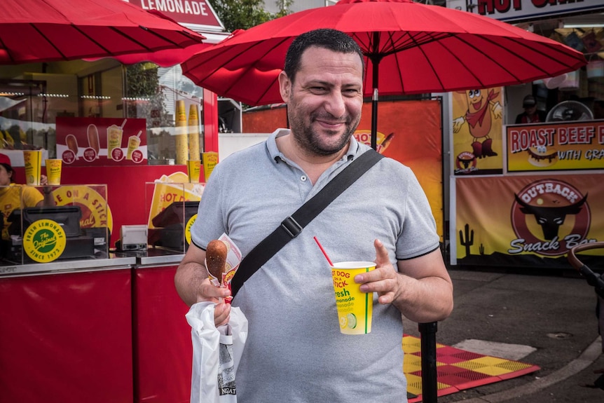 Man attending the Easter Show holds cheese on a stick in one hand and a drink in the other