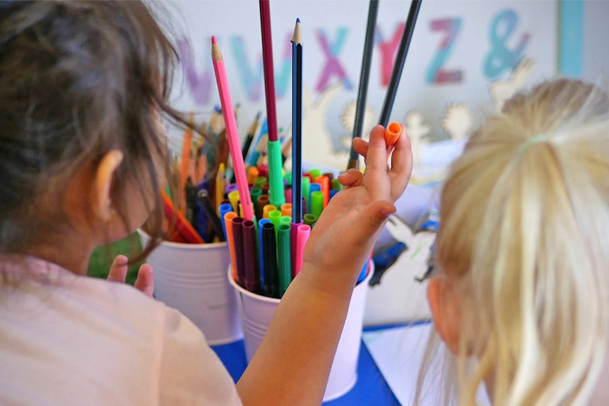 Two female children choose from a tin of coloured textas