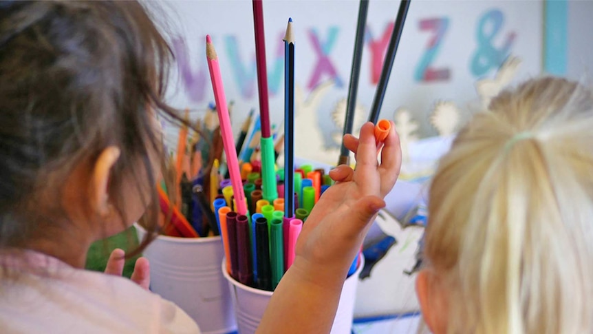 Two female children choose from a tin of coloured textas