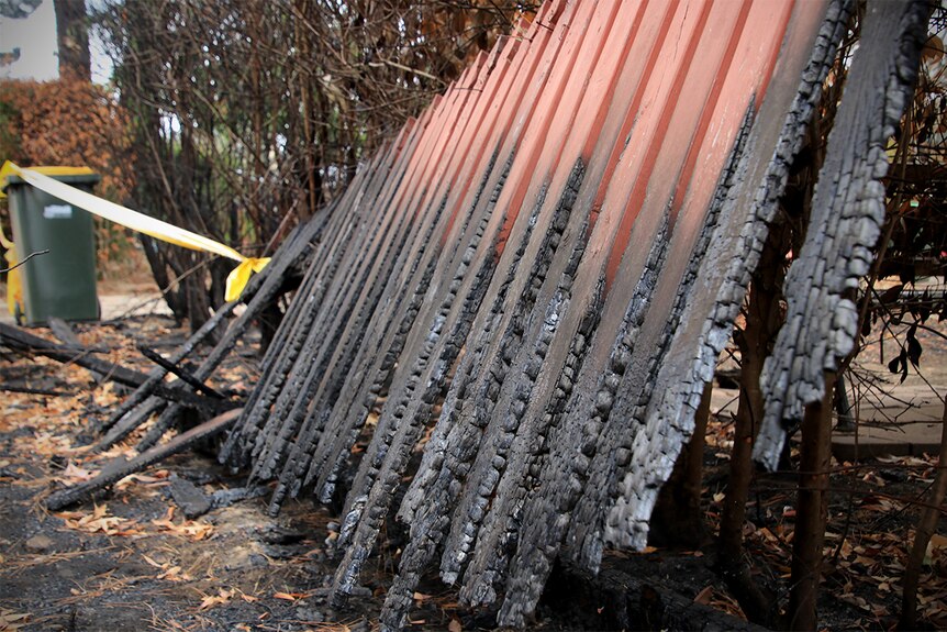 A burnt fence with exclusion tape at a house destroyed by fire.