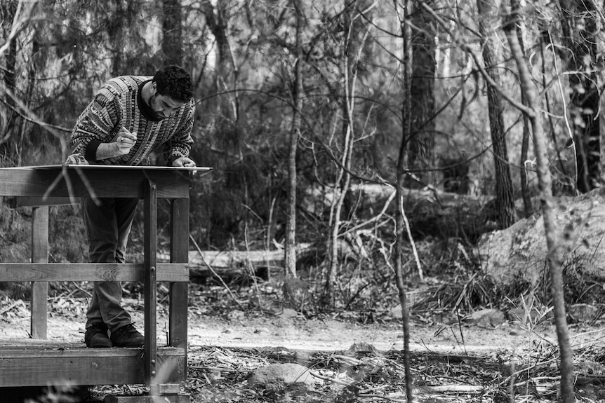 Young man leaning on the rail of a timber lookout writing on a placard