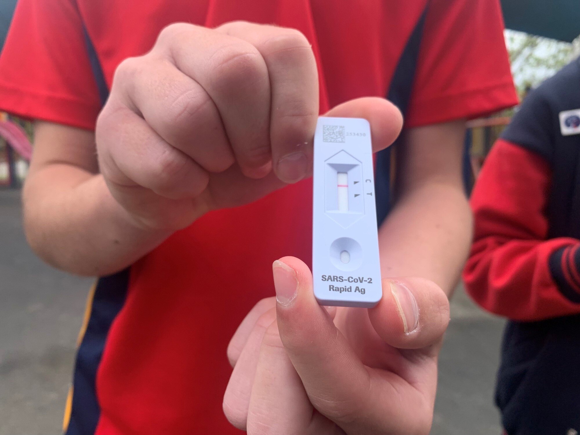 Close-up of hands of boy in red shirt with white testing result.