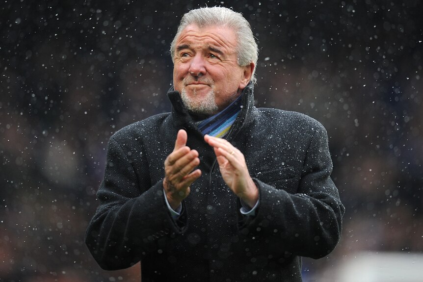 A football manager claps his hands in the snow.
