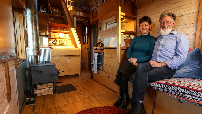 A smiling couple sit inside a cosy room in a small house
