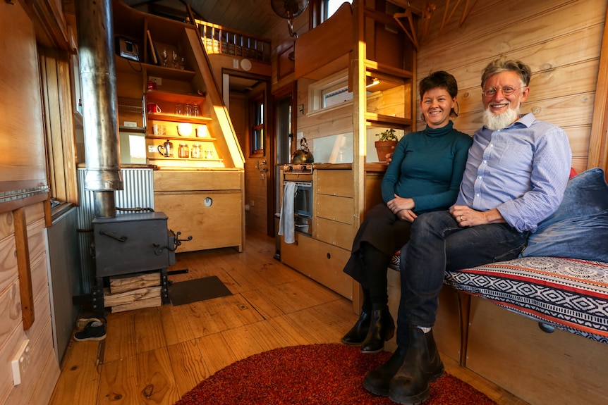 A smiling couple sit inside a cosy room in a small house