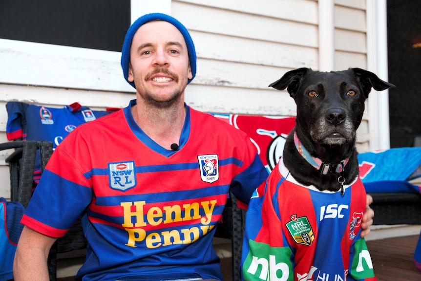 a man and his dog sitting next to eachother. They are both wearing Newcastle Knights jerseys