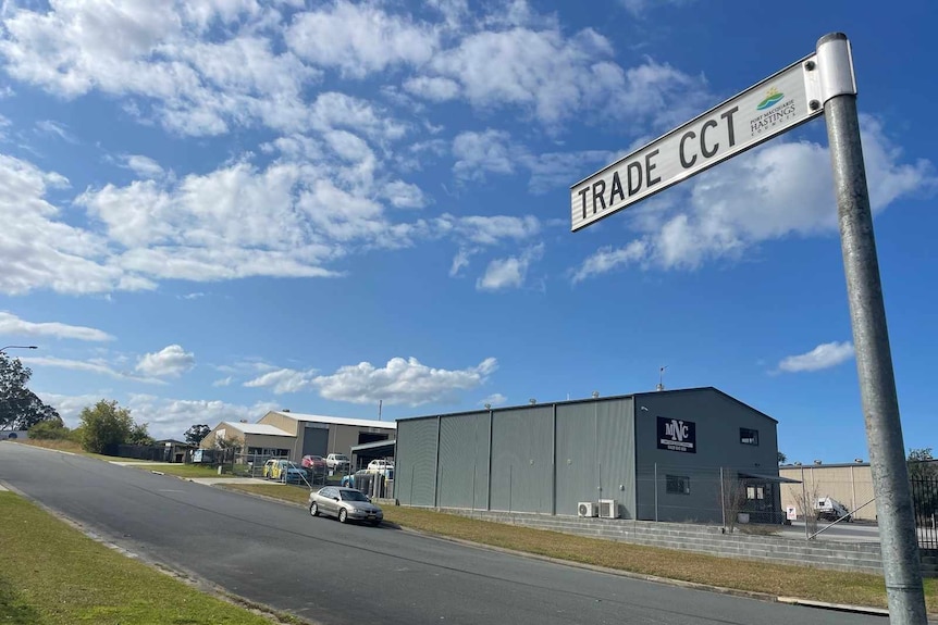 Photo of a street sign reading 'Trade CCT' with a warehouse and car in background