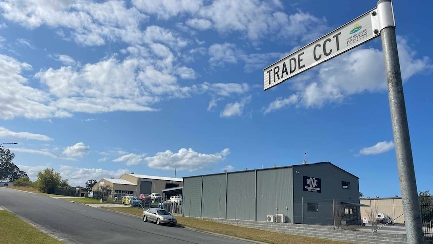 A street sign that reads "Trade CCT" with a warehouse and car in background.