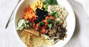 Taco bowl with carrots, corn, quinoa, spiced meat, cherry tomatoes, cheese, corn chips, guacamole and beans from our recipe