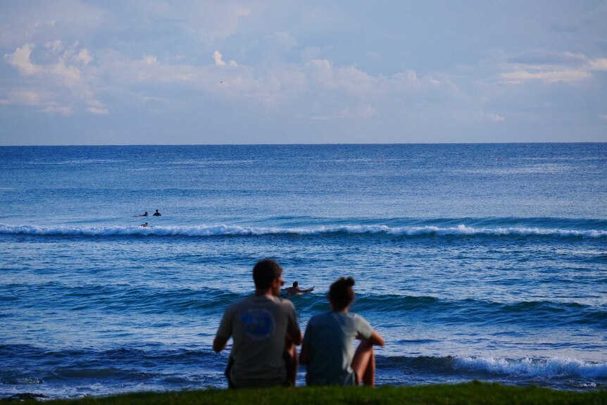 Two people sit on a hill overlooking the ocean at Burleigh Heads.