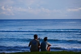Two people sit on a hill overlooking the ocean at Burleigh Heads.