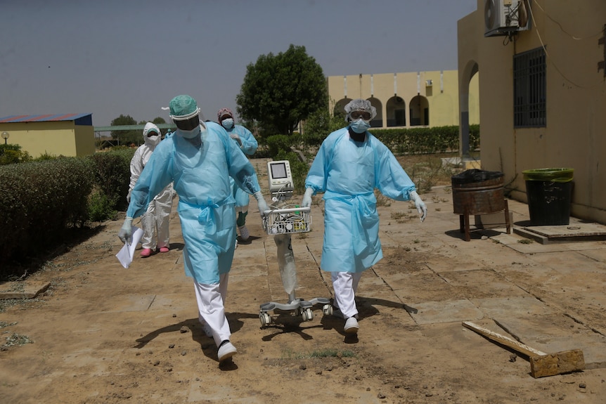 Doctors in personal protective equipment wheel a cart into a hospital in Chad.