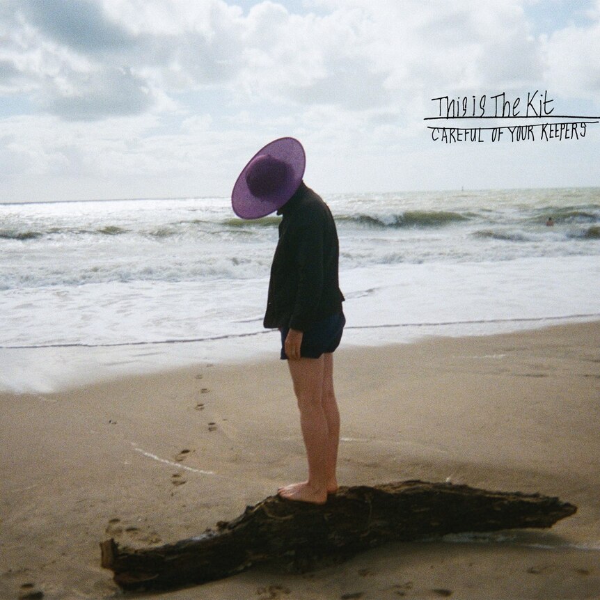 a woman wearing a purple hat stands on the shore of a beach looking down