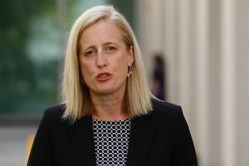 Senator Gallagher has long blonde hair and is wearing a black blazer. She's standing in a courtyard.