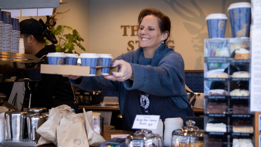 A woman hands over a tray of takeaway coffees at a cafe.