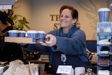 A woman hands over a tray of takeaway coffees at a cafe.