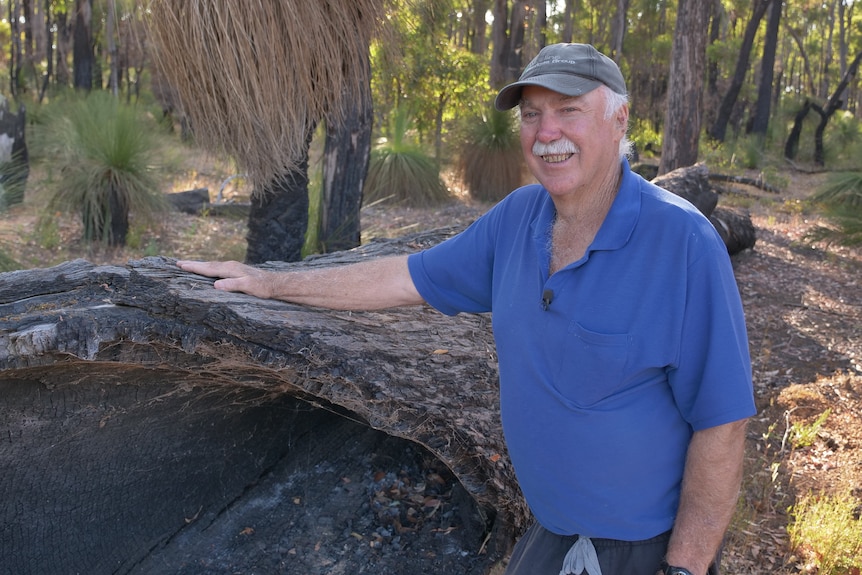 Bill Smart stands in the forest in a blue polo shirt and grey cap. 