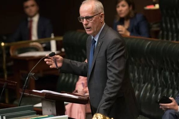 A man wearing glasses talking while standing up at the floor of parliament.