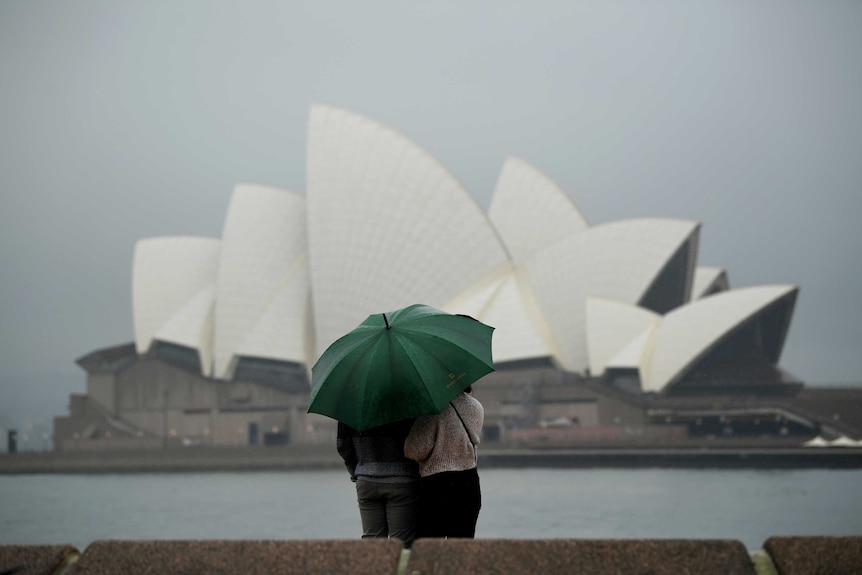 two people huddled underneath an umbreall looking at the sydney opera house