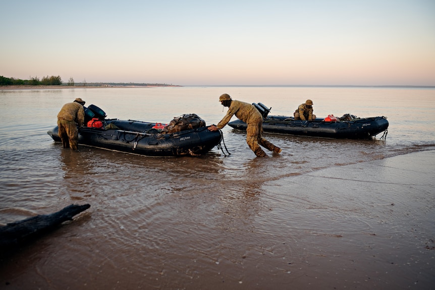 three army personnel pushing inflatable boats out into the ocean