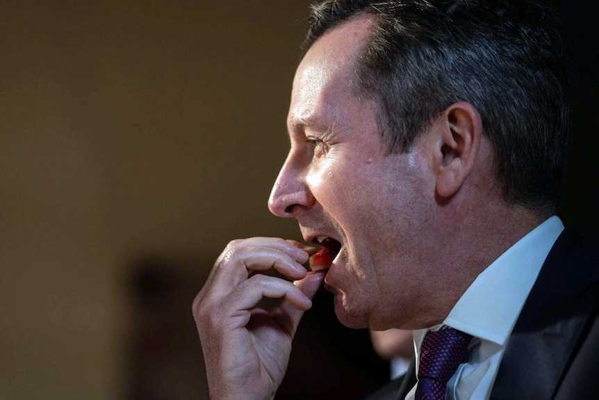 A side shot of Mark McGowan about to bite into a piece of strawberry.