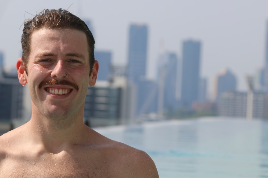 a man smiling, with beads of water on his face and shoulders, fresh from a swim