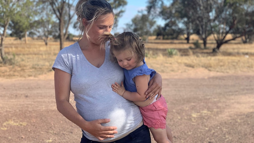 Rebecca stands outside on her farm holding young daughter Mckenna.