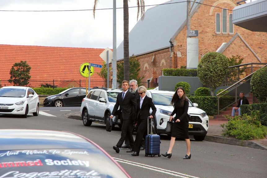 A group of people in suits cross a road in front of a church building