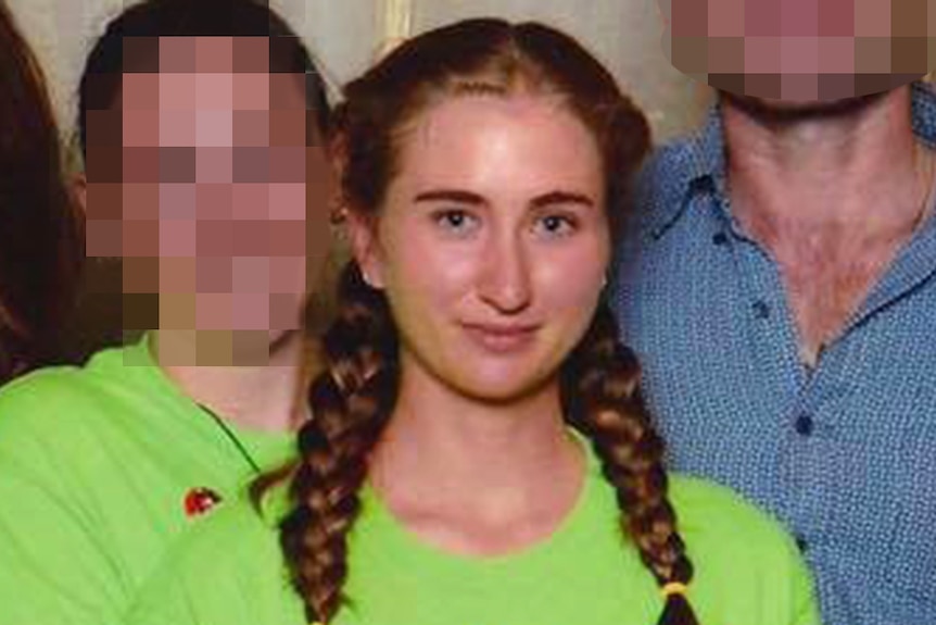 A woman in a green t-shirt with her hair in two plaits poses with other people whose faces are pixellated at an event.